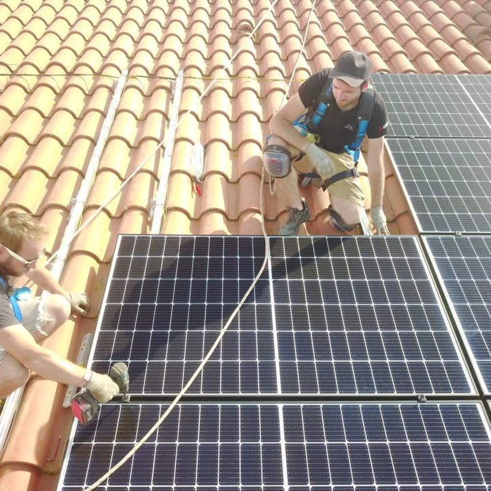 Technicien Elec Froid fixant des panneaux photovoltaïques sur une toiture en tuiles